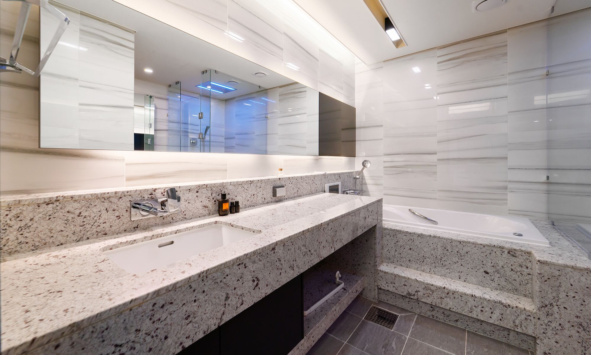 A modern bathroom with a granite countertop, a large mirror, a bathtub, and a shower area.