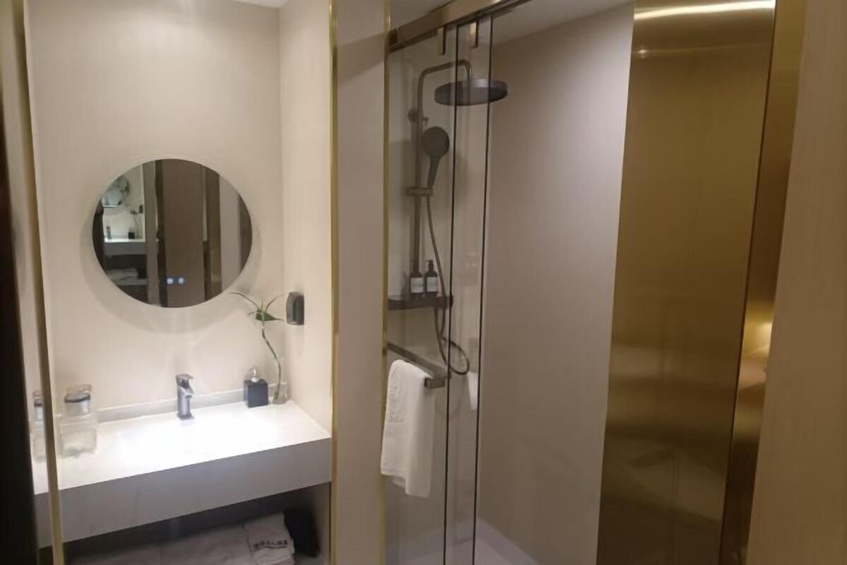 A modern bathroom with a round mirror, a white sink, and a glass-enclosed shower.