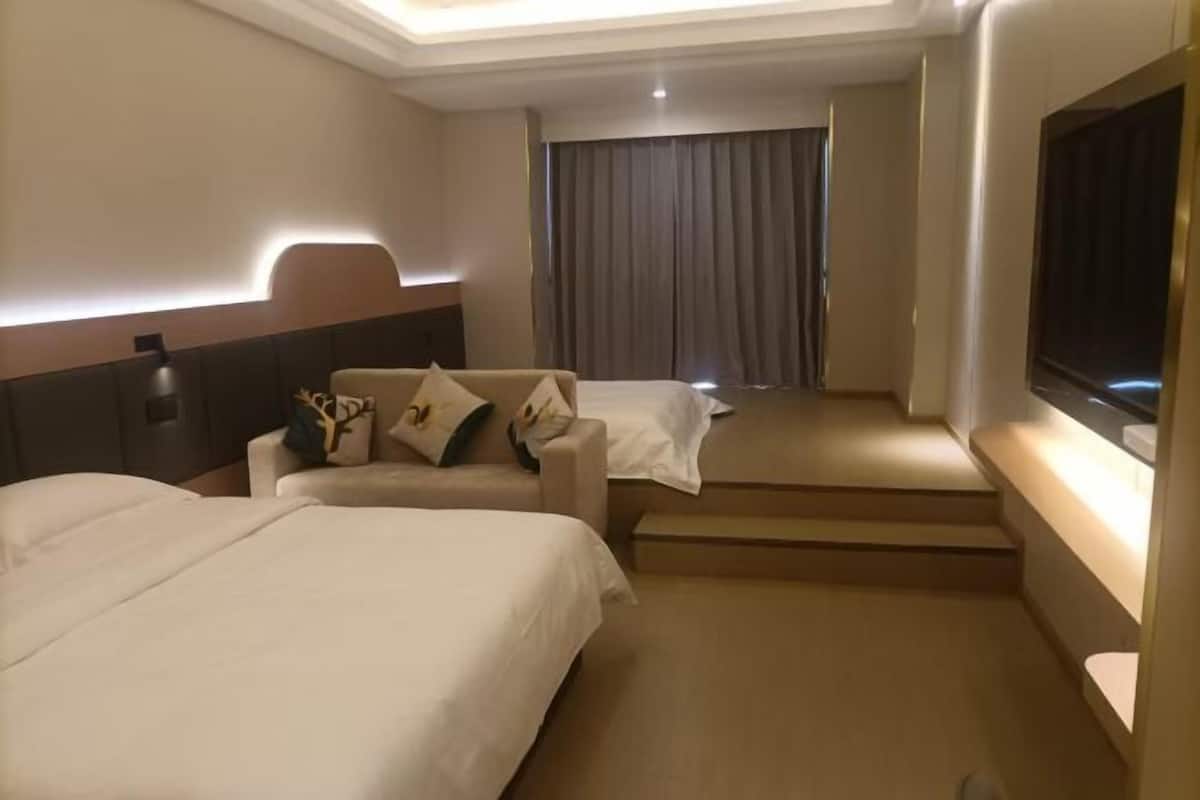 A hotel room with two beds, a sofa, a TV, and a staircase leading to an upper level.