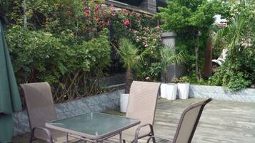 Un patio exterior con mesa y sillas, rodeado de abundante follaje y plantas con flores.