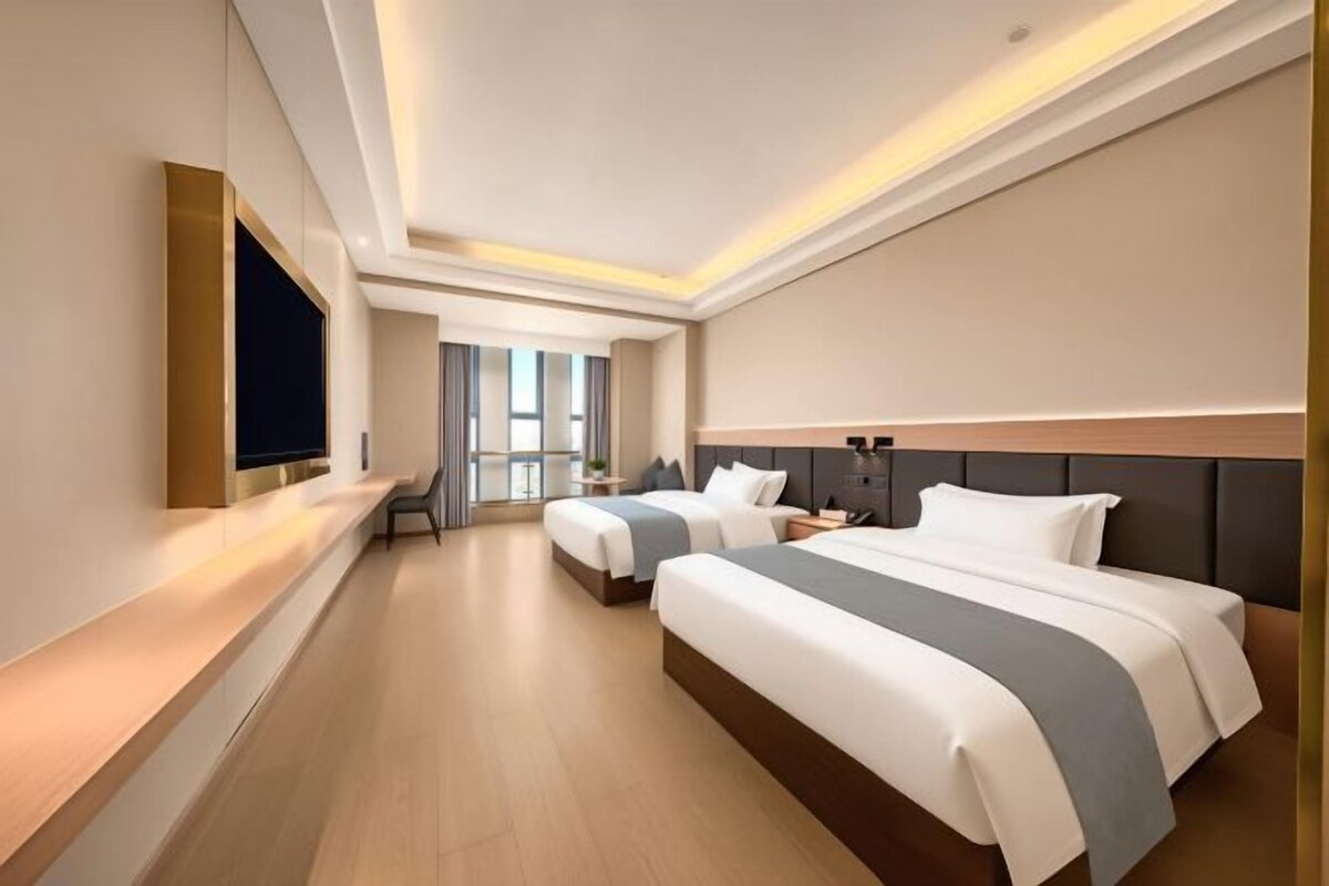 A hotel room with two beds, a flat-screen TV, a bedside table, and a window with curtains.