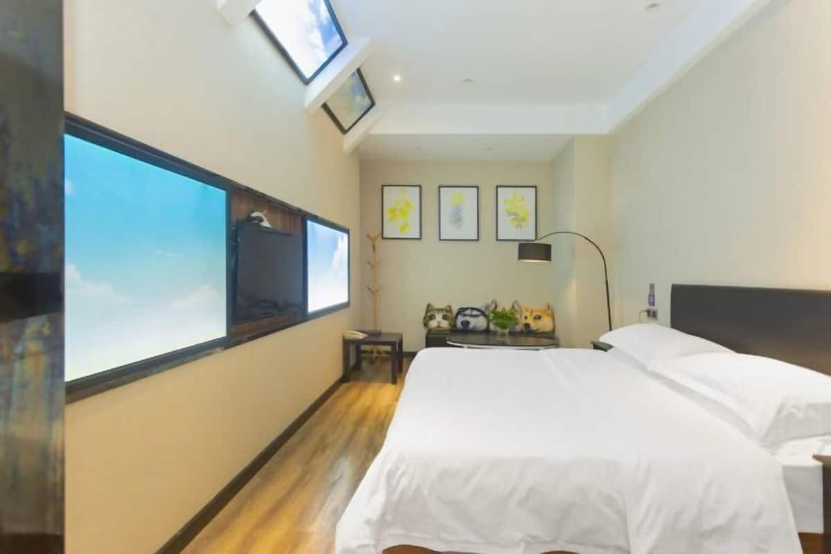 A hotel room with a large bed, a small table, a desk, a chair, a lamp, and a window.