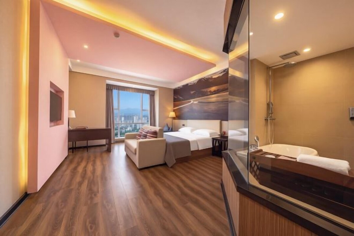 A modern hotel room with a large bed, a sitting area, a bathroom with a bathtub, and a city view.