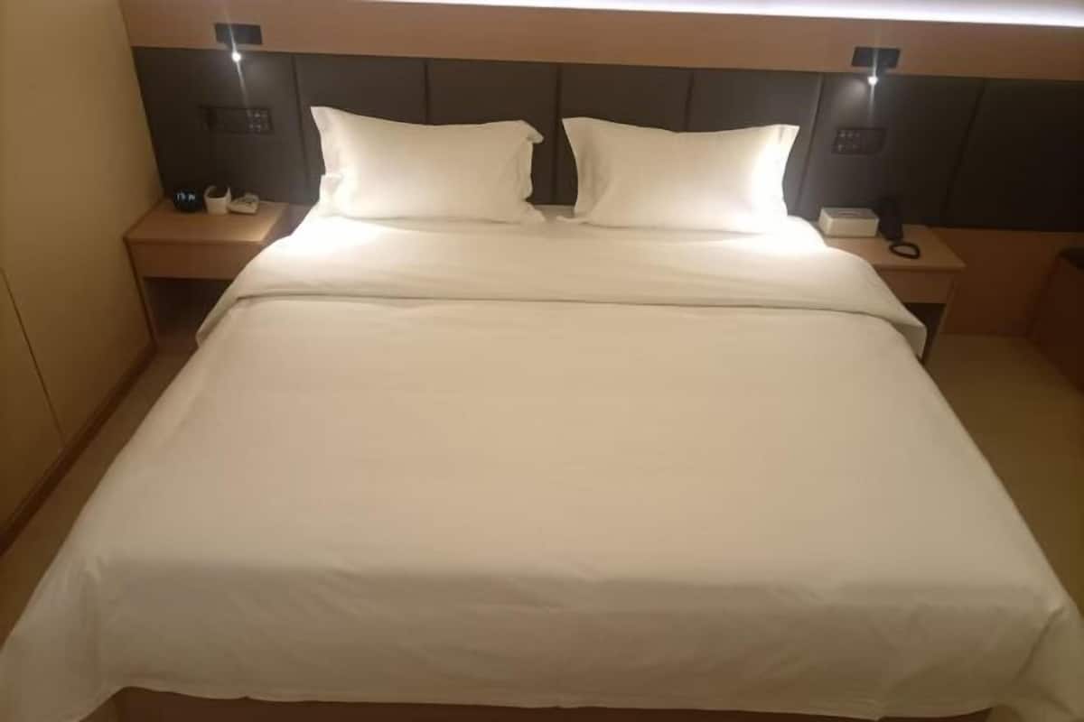 A hotel room with a large bed, bedside tables, and a headboard with built-in lighting.