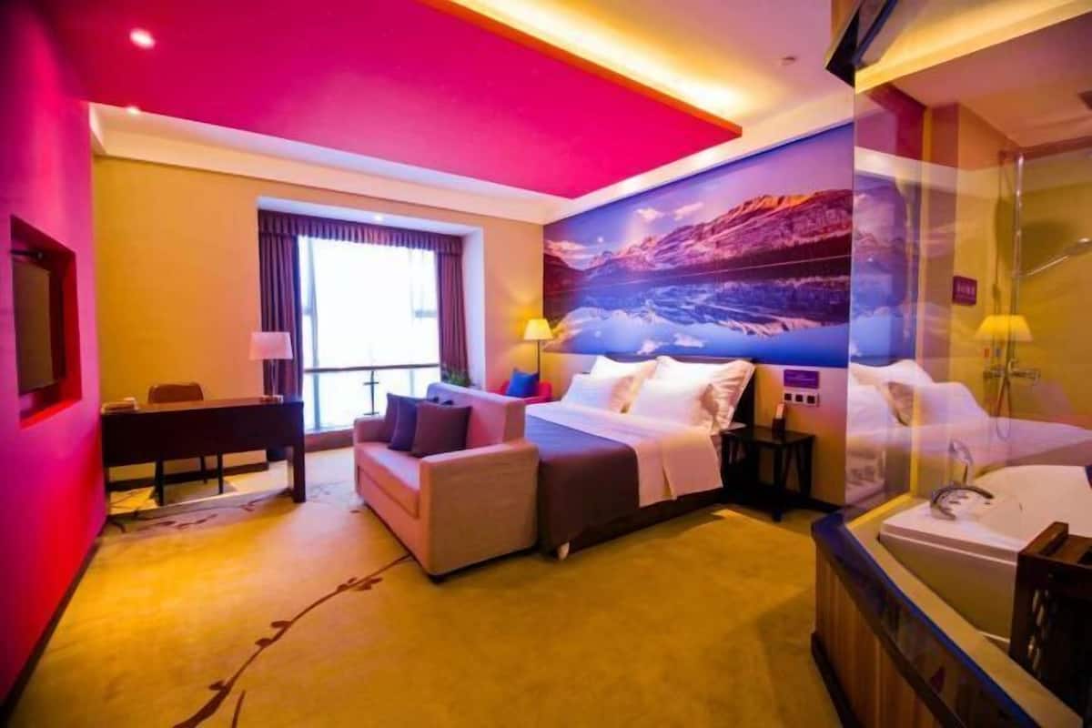 A hotel room with a bed, a desk, a sofa, a window, and a bathroom.
