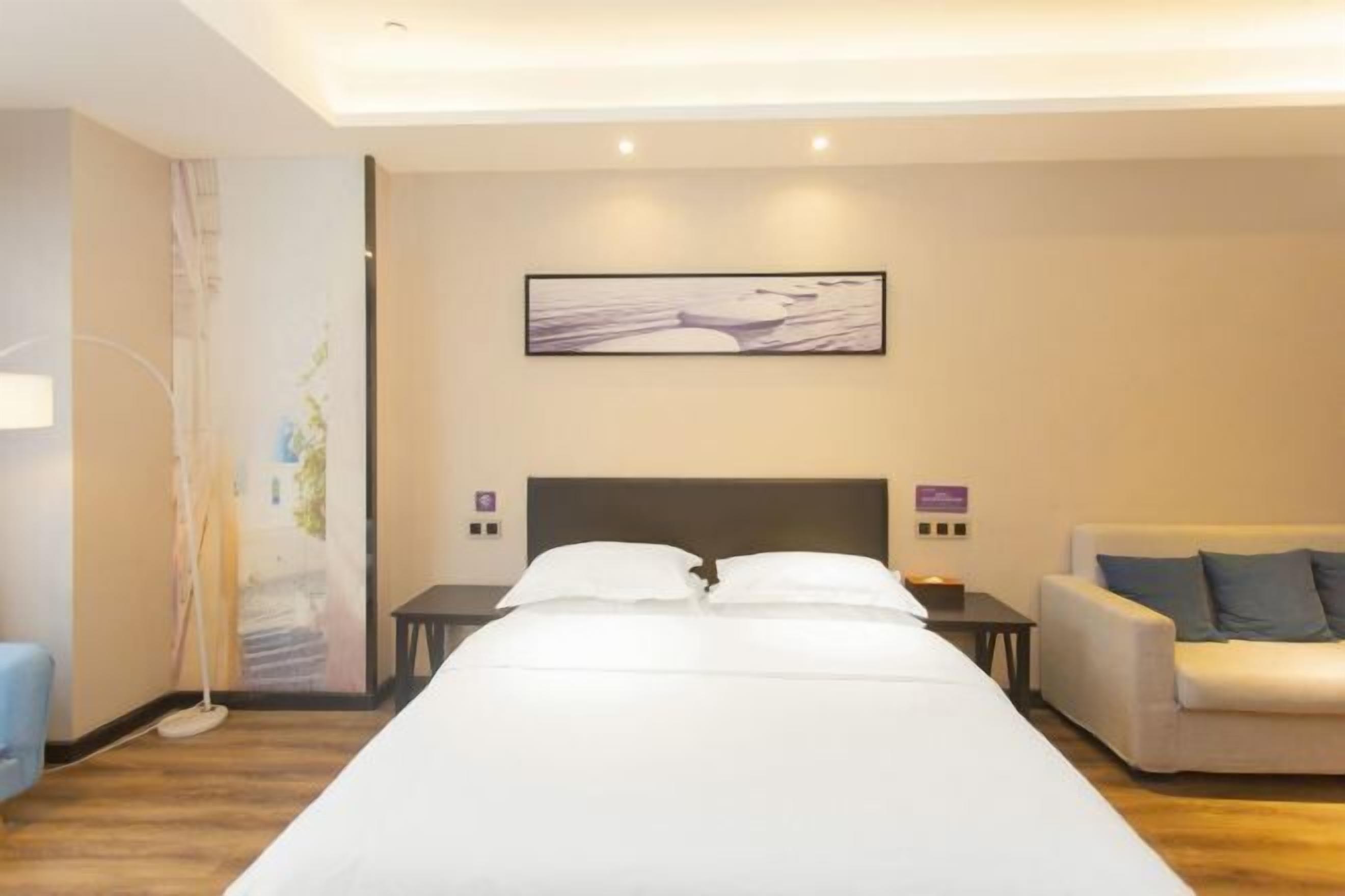 Habitación de hotel con una cama grande, un sofá, una obra de arte en la pared y una lámpara de pie.