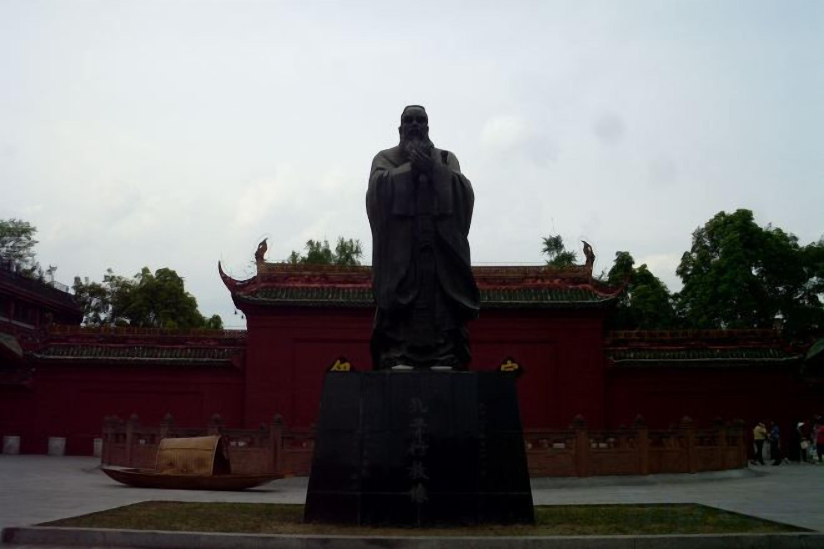 A statue in front of a traditional building with a red roof and a courtyard.