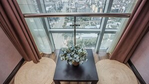 A balcony with a view of a cityscape, a small table with a vase of flowers, and two woven mats. - Platinum Celebrity Hotel (Chongzhou)