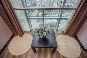 Un balcón con vistas a un paisaje urbano, una pequeña mesa con un florero y dos esteras tejidas.