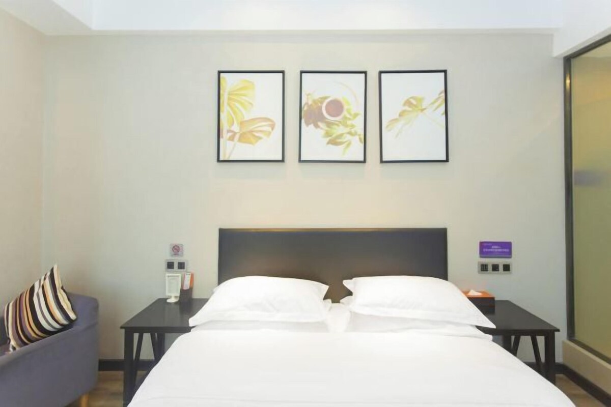 Habitación de hotel con cama, mesita de noche, una silla y tres cuadros en la pared.