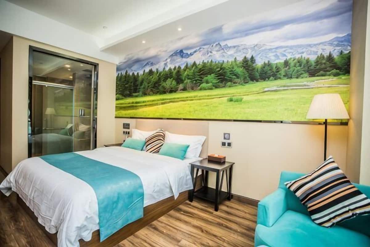 A bedroom with a bed, a nightstand, a lamp, a window, and a wall-mounted painting.