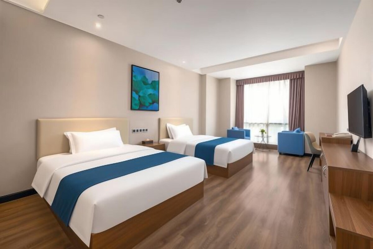 A hotel room with two beds, a desk, a chair, a TV, and a window with curtains.