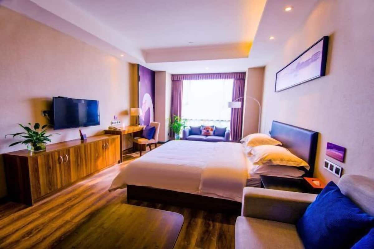 A modern hotel room with a bed, a desk, a TV, and a view of the outside.