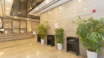 Una zona de recepción con piso de mármol, un mostrador de recepción y varias plantas en macetas.