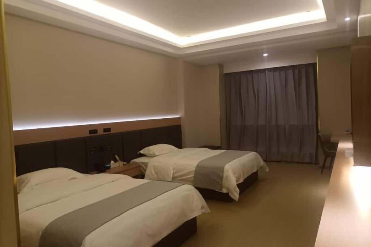 A hotel room with two beds, a desk, a chair, and a large window with curtains.