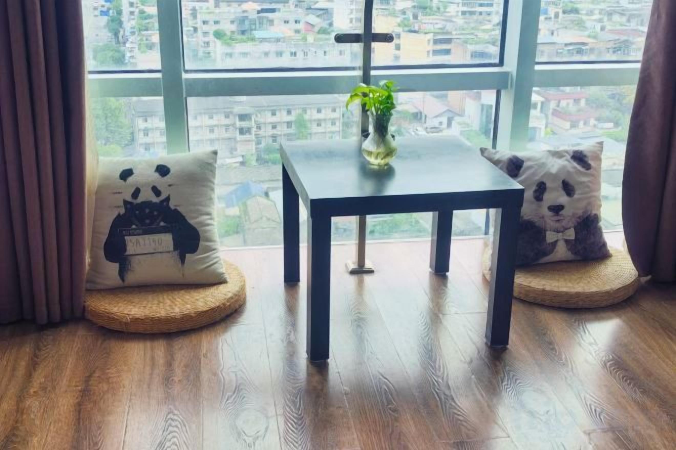 A room with a view through a window, a small table with a plant, and two cushions with animal designs.