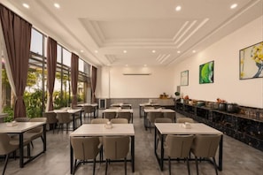 A hotel dining area with multiple tables and chairs, a kitchen counter, and artwork on the walls. - Platinum Celebrity Hotel (Chongzhou)