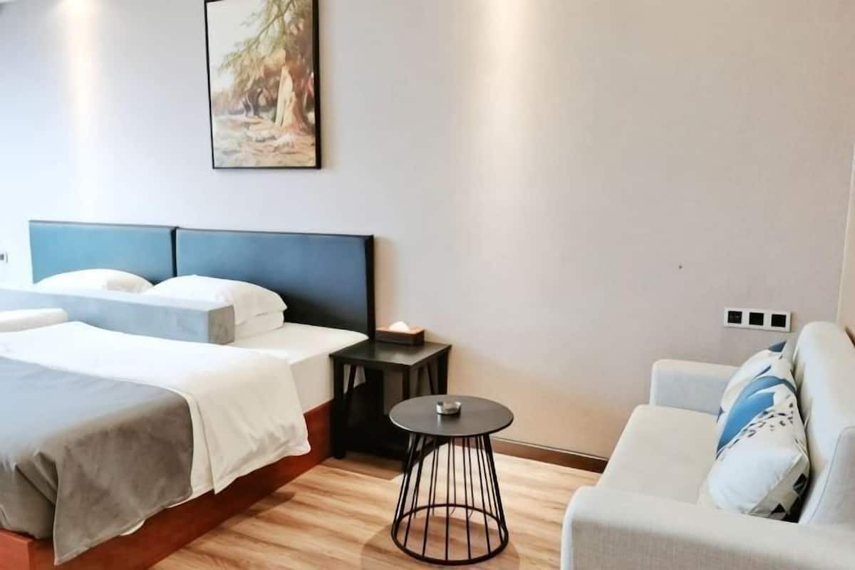 A hotel room with a bed, a sofa, a small round table, and a wall-mounted power outlet.