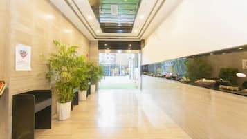 A hotel lobby with a marble floor, potted plants, and a reception desk.
