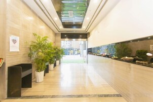 Um saguão de hotel com piso de mármore, plantas em vasos e um balcão de recepção.