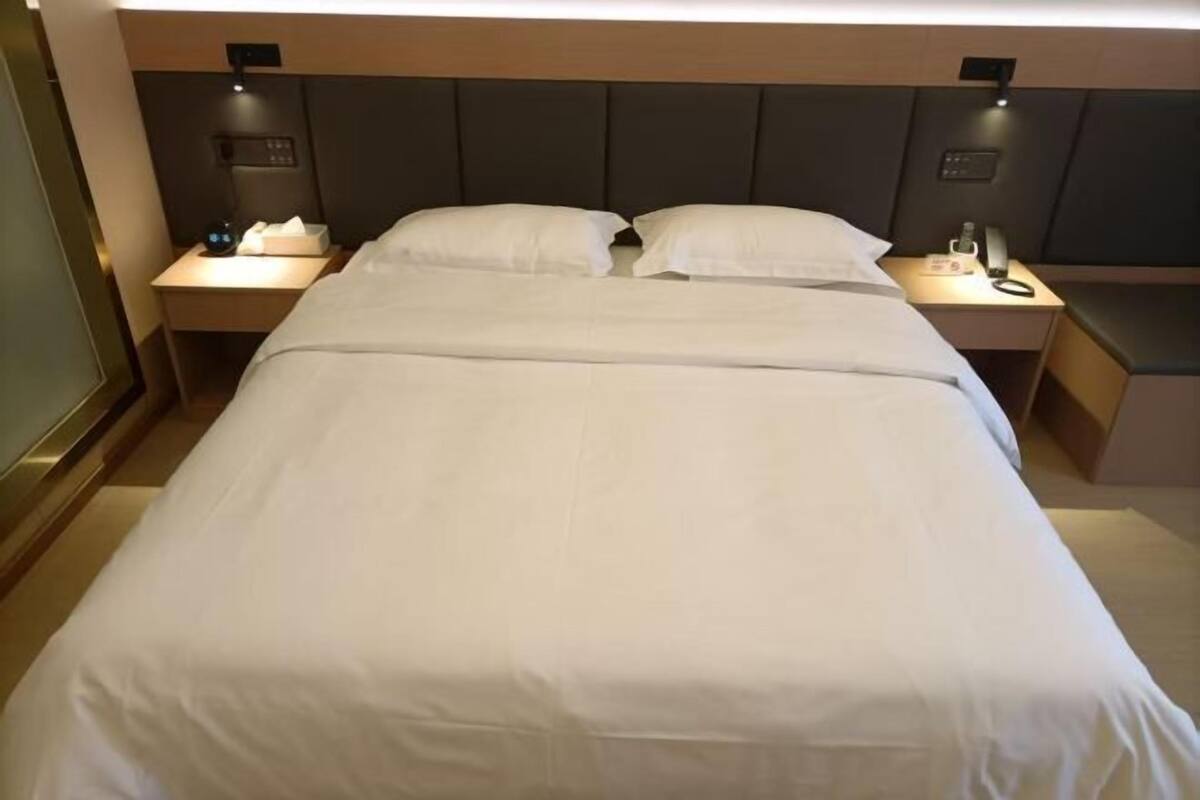 A hotel room with a large bed, bedside tables, and wall-mounted lighting.