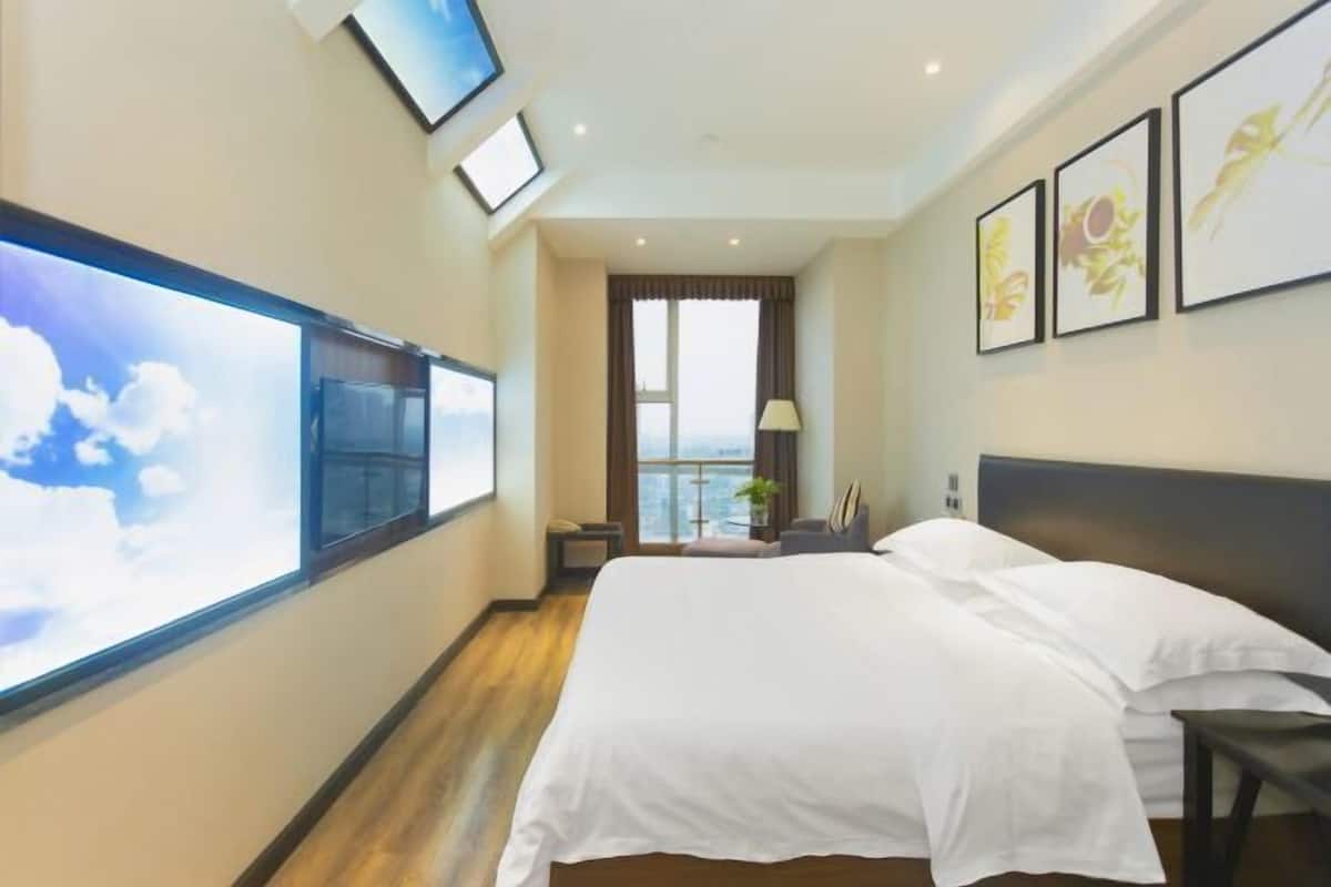 A hotel room with a large bed, a TV mounted on the wall, a window with a view, and framed artwork on the wall.