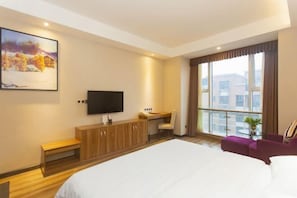 Habitación de hotel con una cama grande, un escritorio, una silla, un televisor y una ventana con vistas a edificios.