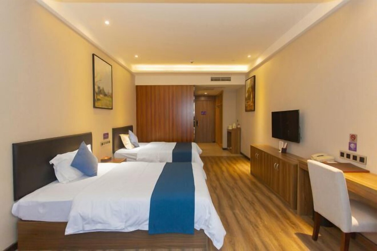 Habitación de hotel con dos camas, un escritorio, una silla, un televisor y una puerta que da a un baño.