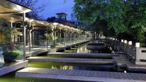 A riverside walkway with glass railings, a covered seating area, and a small bridge over the water. - Tiandi Renhe Luochenghui Hotel (Guanghan)