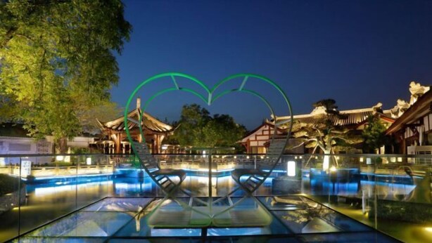 A swimming pool with a heart-shaped glass structure in the center, surrounded by traditional architecture. - Tiandi Renhe Luochenghui Hotel (Guanghan)