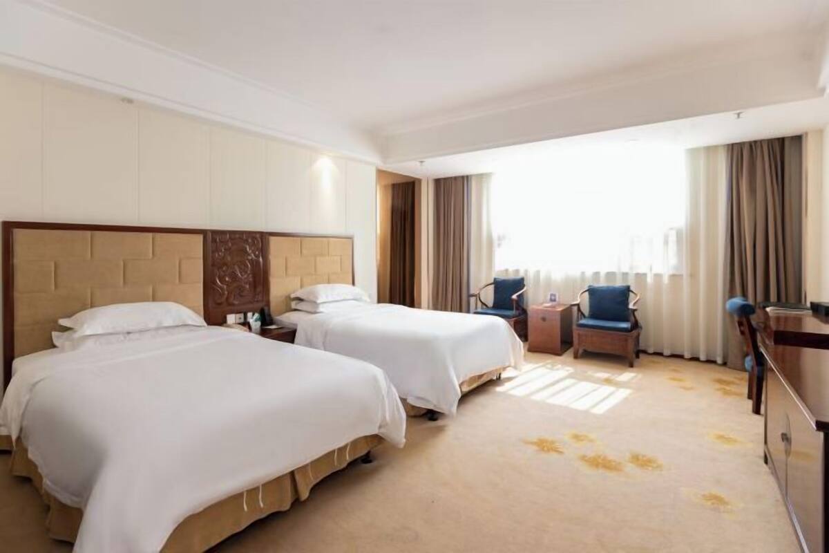 Habitació d'hotel amb dos llits, un escriptori, una cadira i una finestra gran amb cortines.