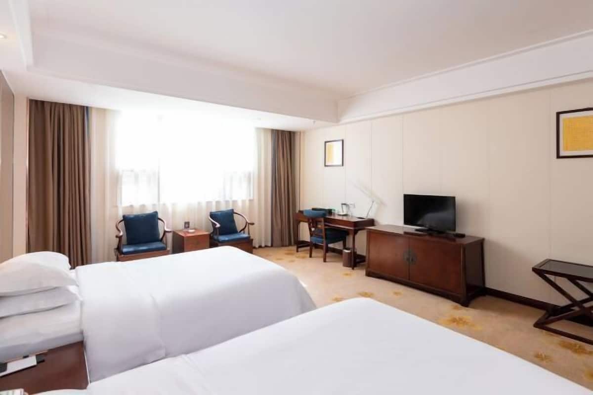 Habitació d'hotel amb dos llits, escriptori, cadira, televisió i finestra amb cortines.