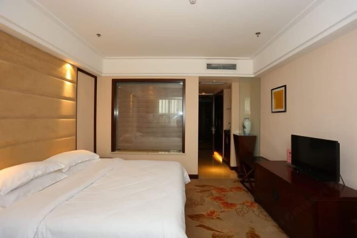 Habitació d'hotel amb un llit, televisió, escriptori i una porta que dona a un passadís.