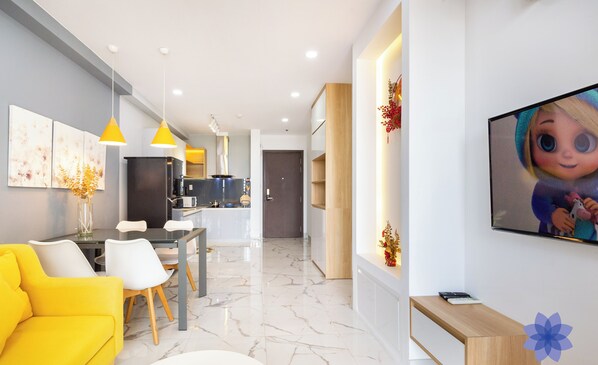 Un salon moderne avec un canapé jaune, un coin repas et une cuisine en arrière-plan.