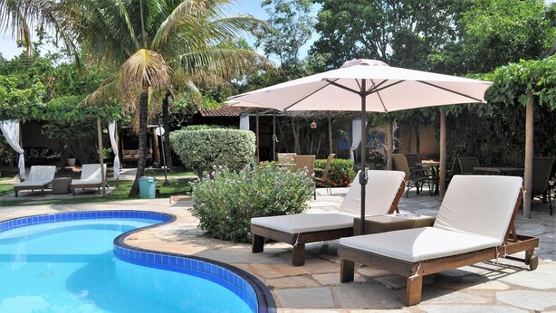 A poolside area with lounge chairs, a covered umbrella, and a swimming pool.
