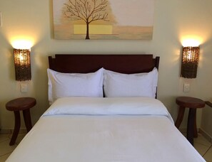 Een hotelkamer met een groot bed, twee nachtkastjes, een wandlamp en een schilderij van een boom.