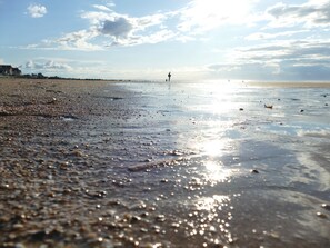 Una playa con arena mojada y una persona caminando a lo lejos.