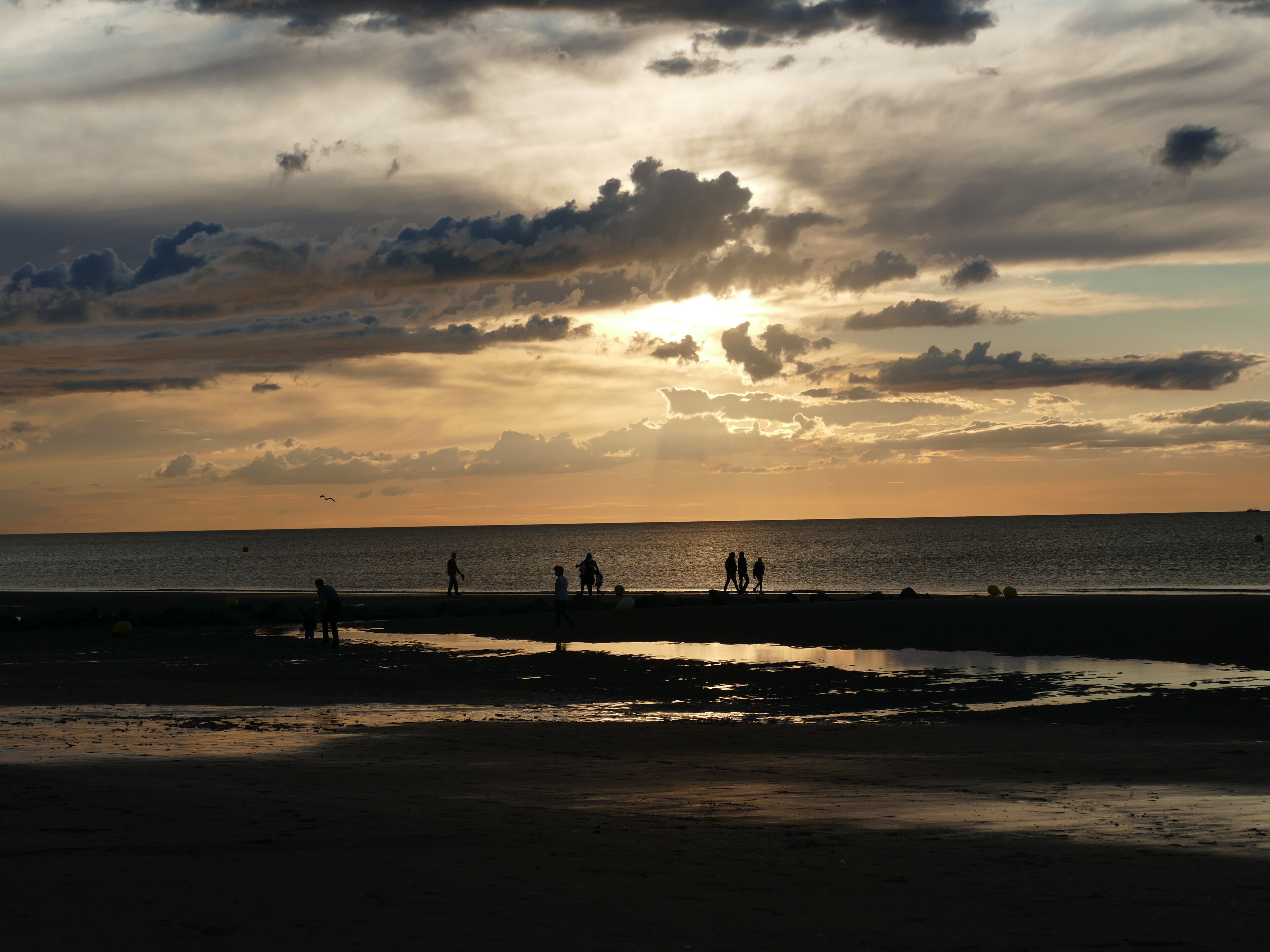 Une scène de plage où l’on voit des personnes se promener le long du rivage au coucher du soleil.