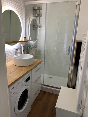 Enjoy a clean and functional bathroom with a washing machine, glass-enclosed shower, and spacious sink area.