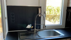 A modern kitchen with a black countertop, stainless steel sink, and wooden cabinets. - Garden level T2+Cabin direct access to the sea (Cabourg)