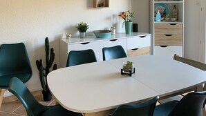 A dining area with a white table and teal chairs, a cactus on the floor, and a white cabinet with shelves against the wall. - Garden level T2+Cabin direct access to the sea (Cabourg)