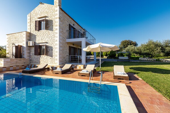 A poolside area with lounge chairs and a clear blue pool, surrounded by a stone building with a balcony.