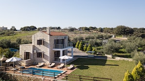 A stone villa with a pool, outdoor seating, and a view of the surrounding landscape.