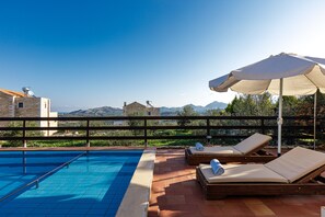 A rooftop pool with two sun loungers and an umbrella, overlooking a mountainous landscape.