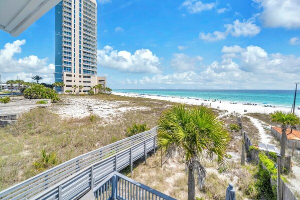 A beach with a high-rise building, sandy shore, and a pedestrian walkway.