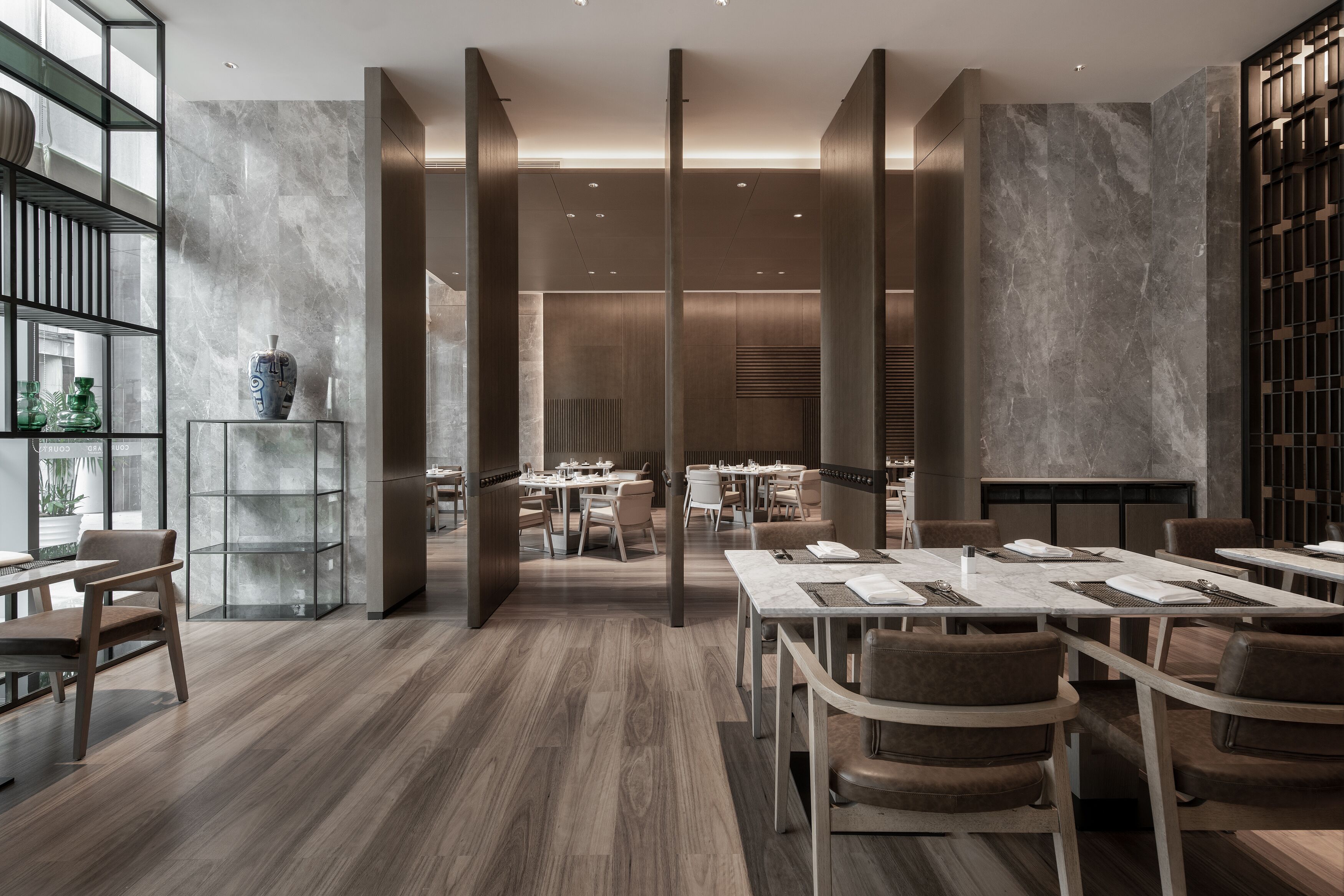 Un comedor moderno con mesas y sillas altas, un expositor de vidrio y vista a un salón de comidas.