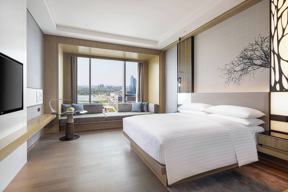A modern hotel room with a large bed, a seating area with a view, and a flat-screen TV.
