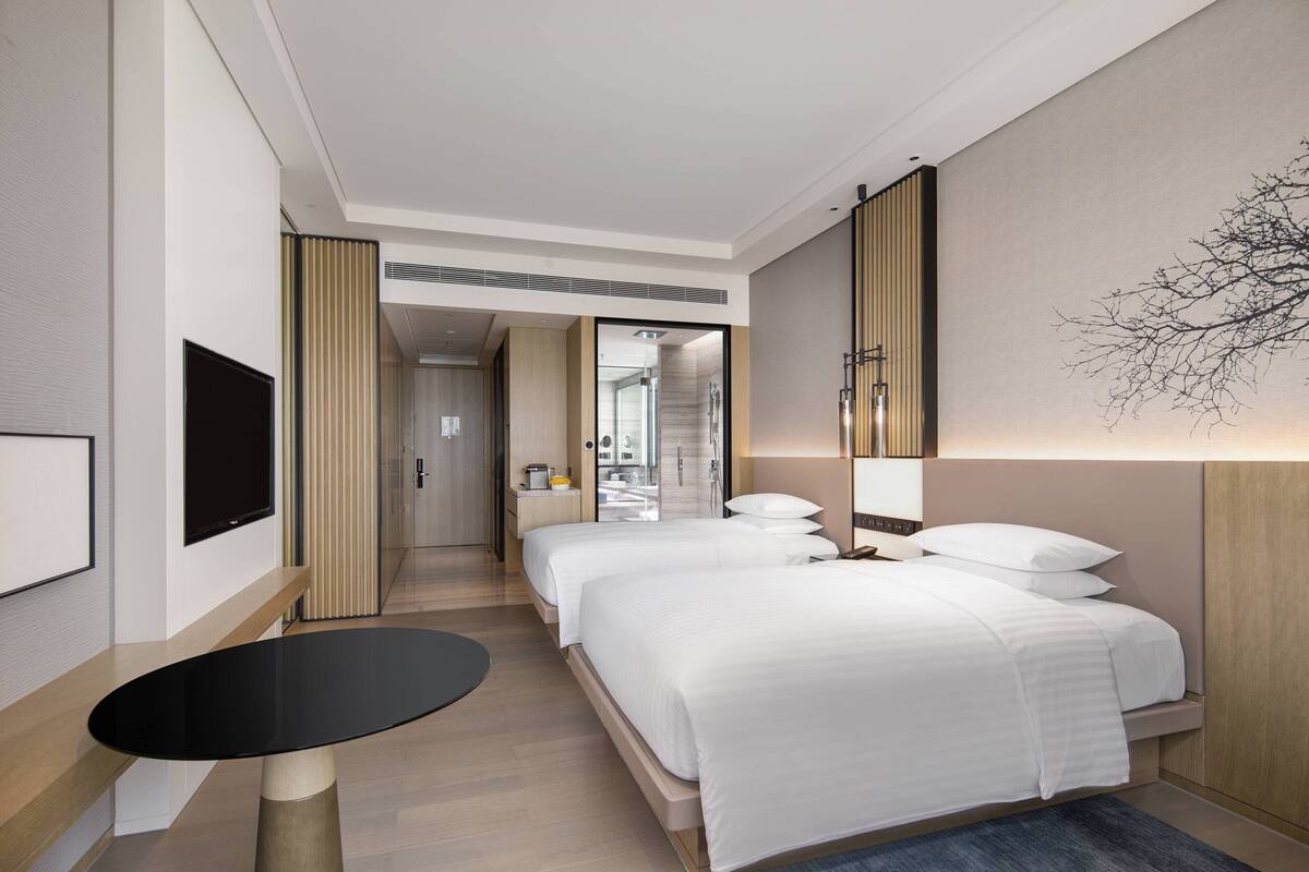 A hotel room with two beds, a flat-screen TV, a small round table, and a large mirror.