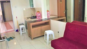 A room with a wooden cabinet, a red chair, a white stool, and a small table with items on it. - Apartement Puncak Permai Tower A by Nur Faizah (Surabaya)