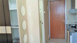 A bedroom with a bed, a wardrobe, a door, and a kitchenette area. - Apartement Puncak Permai Tower A by Nur Faizah (Surabaya)